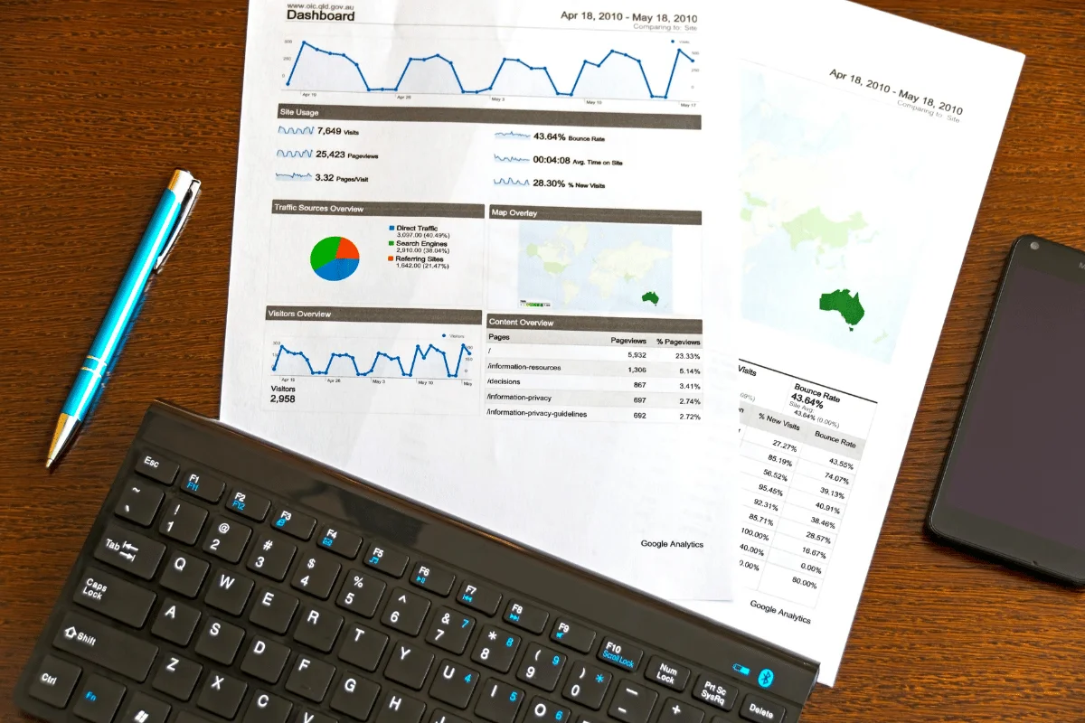 Printed Google Analytics dashboard report with charts, keyboard, and pen on desk.