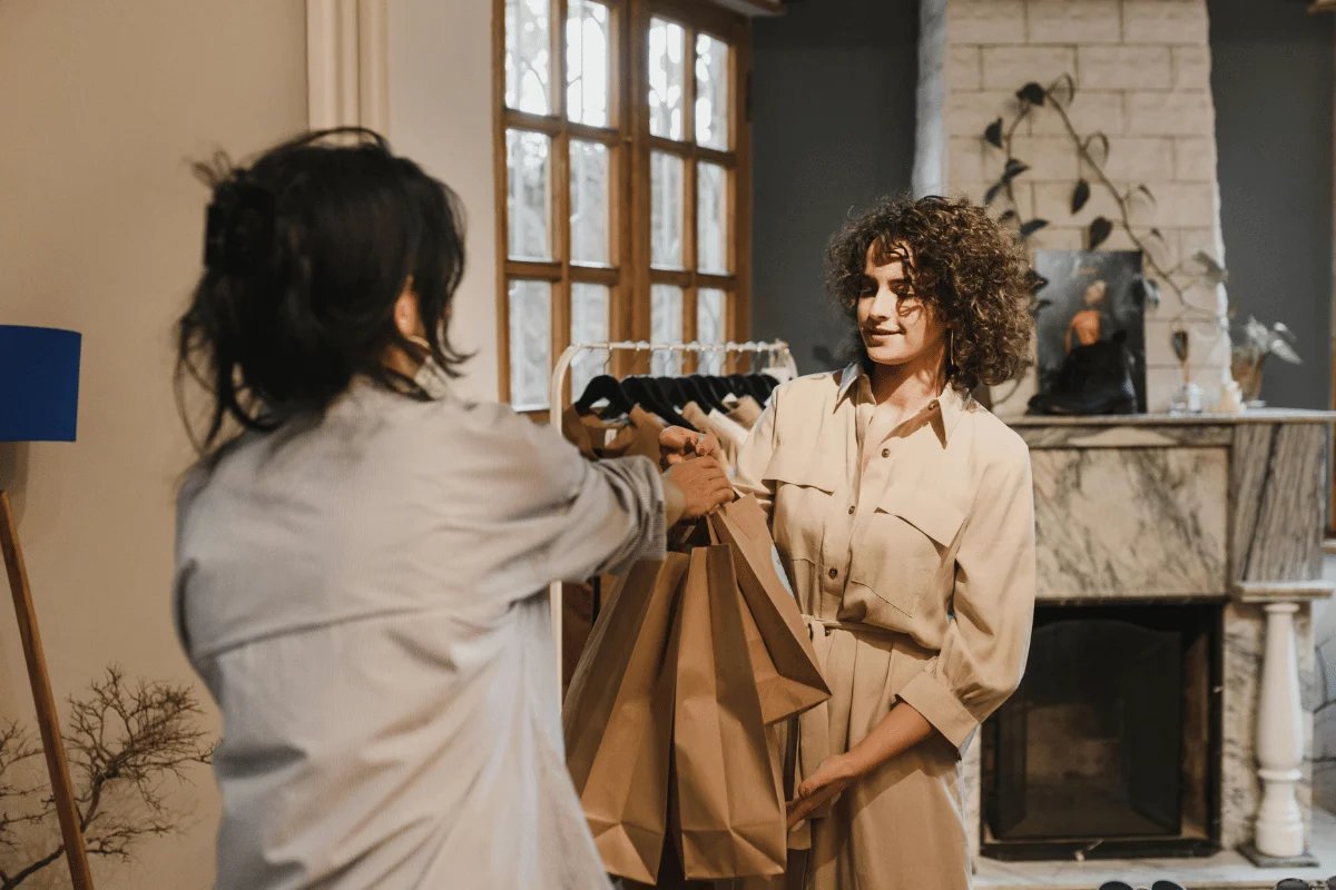 Two women exchanging shopping bags inside a boutique, representing in-store retail experience and customer service.