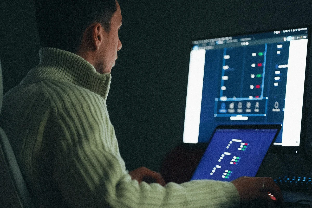 Developer working late analyzing software interface on dual monitors in dark office environment.